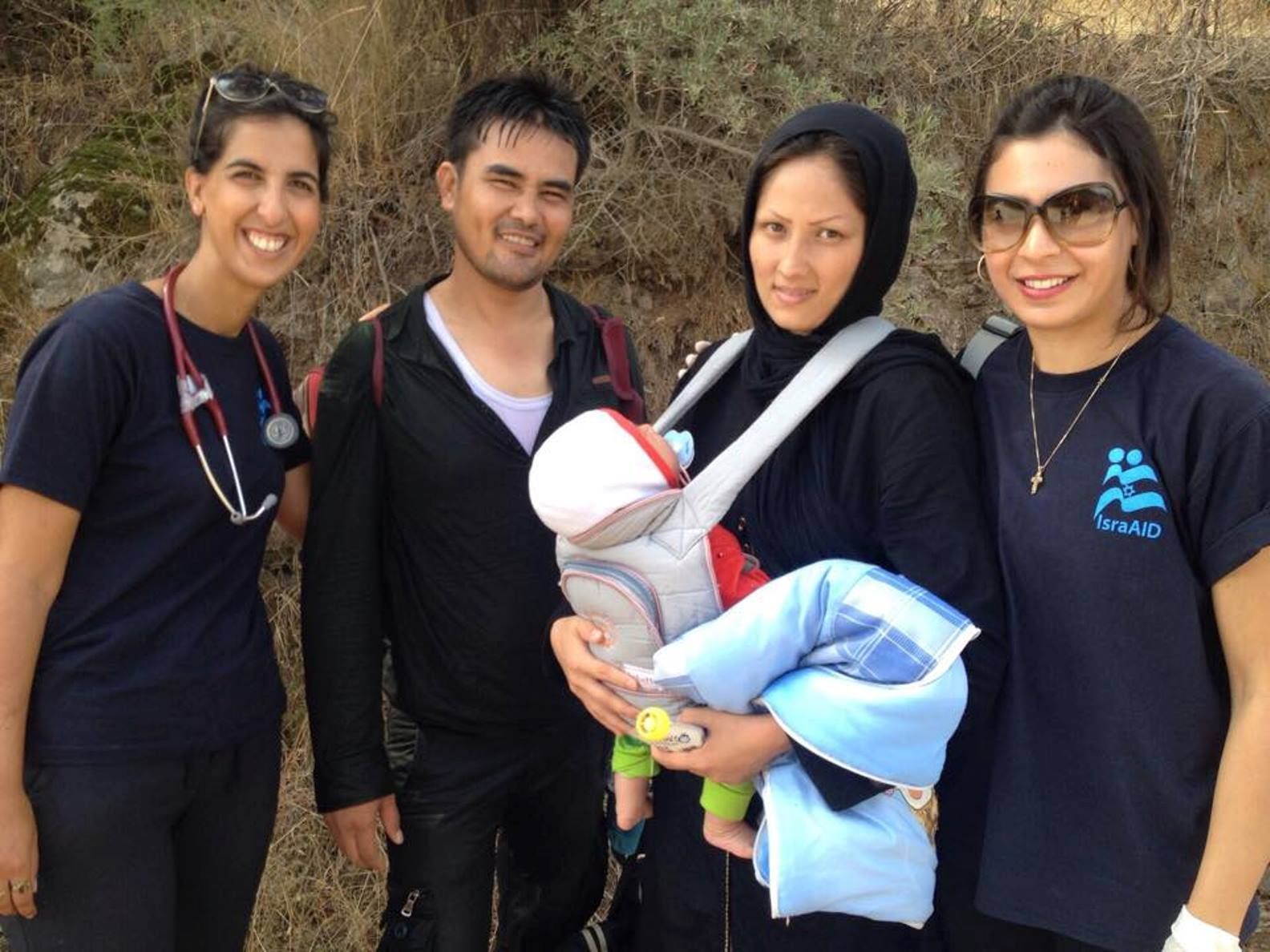Jewish Israeli and Arab Israeli IsraAID volunteers flank a refugee couple to whom they gave a baby carrier. Photo via Facebook