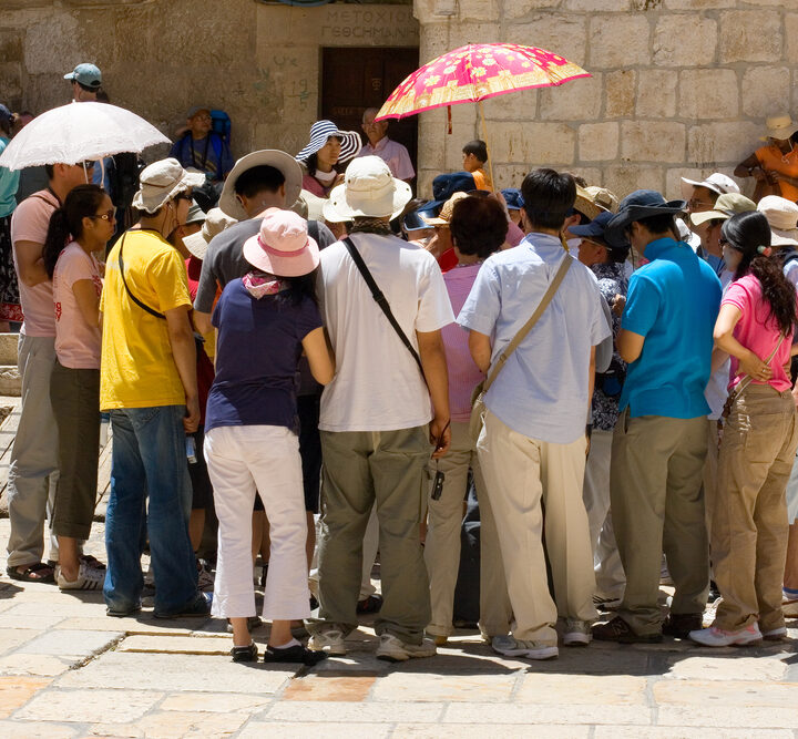 A group of Asian tourists listening to a guide at the entrance of the Church of The Holy Sepulcher, Jerusalem. Photo via Shutterstock.com