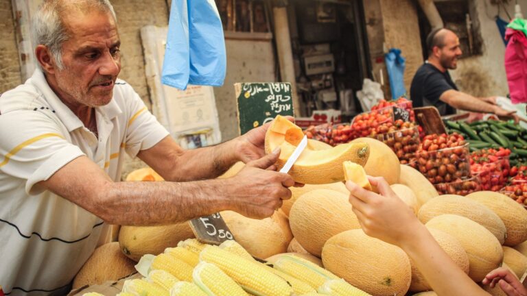 A stall owner cuts a piece of melon for a customer at Machane Yehuda market in Jerusalem. Photo by Garrett Mills/Flash90