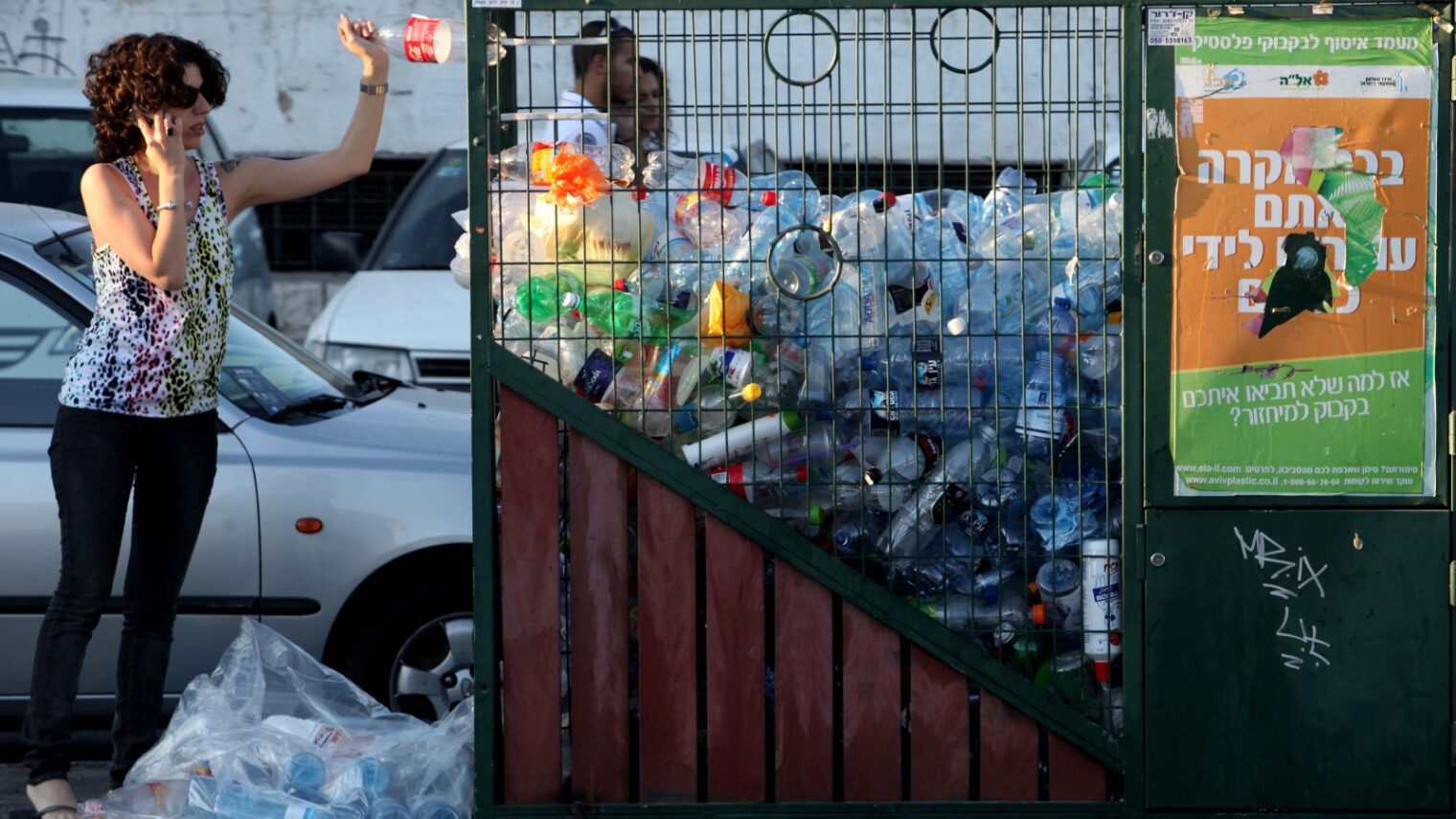 A woman throws a bottle into the recycling bin in Jerusalem. Photo by Nati Shohat/Flash90