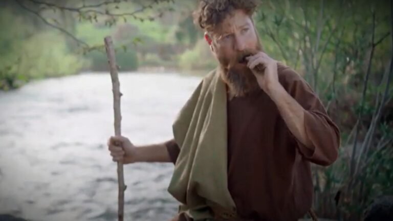 An actor depicts John the Baptist enjoying a locust and honey snack on the banks of the Jordan River. Image: YouTube screenshot/Dror Tamir