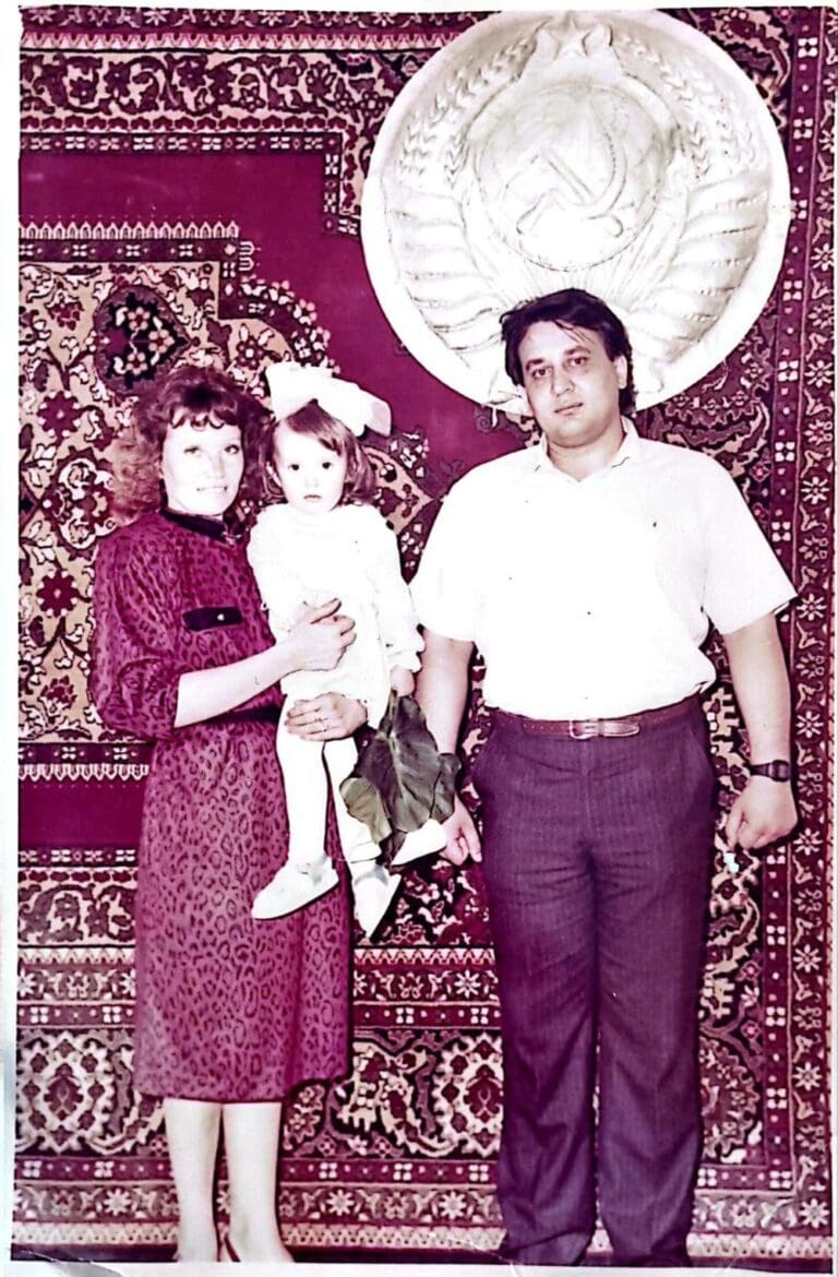 Yulia Karra and her parents in front of a Communist coat of arms and traditional Turkmen rug, circa 1990. Photo courtesy of the family