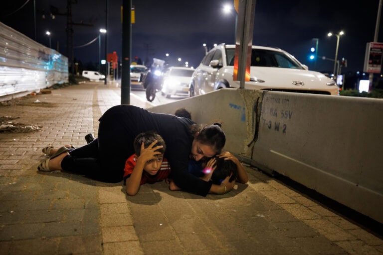 A mother shields her children from Hamas rockets fired over central Israel, October 13, 2023. Photo by Ziv Koren/Polaris Images